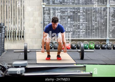 Volle Frontansicht eines passstarken und entschlossenen jungen Mannes, der beim Powerlifting-Training im Fitnessstudio mit dem Deadlift-Training beginnt Stockfoto