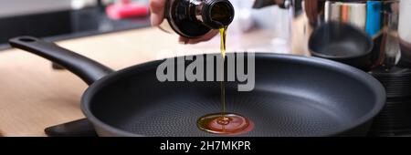 Koch gießt Olivenöl in die Bratpfanne in der Küche aus der Nähe Stockfoto