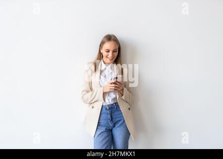 Porträt einer glücklichen Frau mit Smartphone und Blick auf die Kamera, stehend auf weißem Hintergrund. Stockfoto