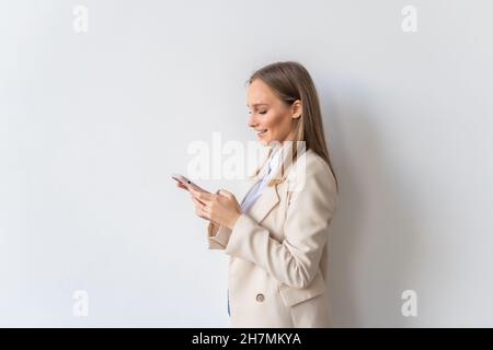Porträt einer glücklichen Frau mit Smartphone und Blick auf die Kamera, stehend auf weißem Hintergrund. Stockfoto