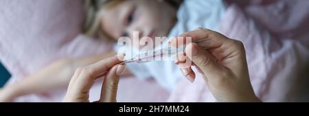 Frau Hand hält Quecksilberthermometer mit hoher Temperatur vor dem Hintergrund von kranken Mädchen Nahaufnahme Stockfoto