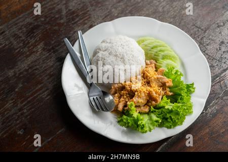 Frittiertes Schweinefleisch mit Knoblauch mit Jasmin-Reis in weißem Teller, Gemüsesalat und Gurke für die Beilage, Thai-Food easy menu, close up imag Stockfoto