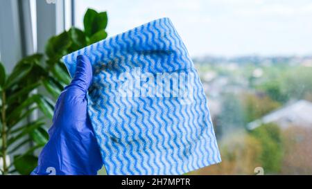Der Mitarbeiter hält einen Gummischutzhandschuh, der schmutziges Mikrofasertuch hält und das Fenster vom Staub abwischt. Allgemeine Frühjahrsputz. Hausarbeit und Housekeeping Stockfoto