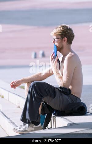 BARCELONA, SPANIEN - 20. Nov 2021: Junger Mann sitzt in einem Park und sonnen sich in Barcelona, Spanien, 20th 2021. November. Stockfoto