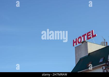 Das rote Neonschild für das HOTEL auf dem Dach des Gebäudes. Grüne Dachfenster und Satellitenschüsseln. Tourismus, Architektur. Selektiver Fokus. Stockfoto