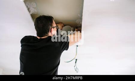 Mann, der Rohr für die Installation der Küchenhaube an der Küchendecke platziert Stockfoto