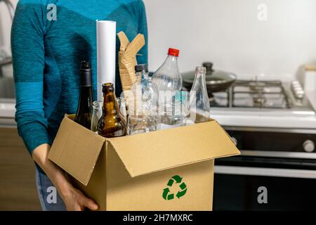 Sortierung und Recycling von Haushaltsabfällen - Frau hält einen Karton mit Plastik-, Glas- und Papiermüll Stockfoto