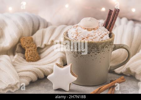 Tasse Kaffee oder heiße Schokolade mit Creme, Zimt und weihnachtskeksen, Lichterketten im Hintergrund Stockfoto