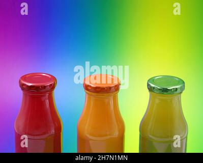 Glasflaschen mit gesunden Smoothies auf buntem Hintergrund mit Kopierraum, Nahaufnahme von roten, orangefarbenen und grünen Saftflaschen Stockfoto