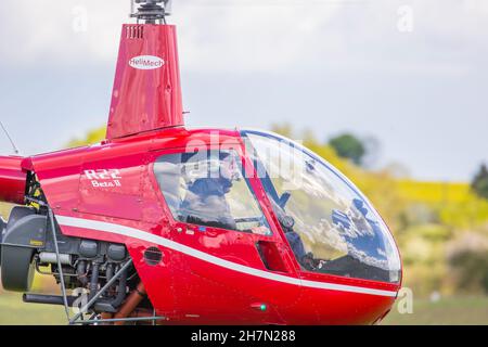 Seitenansicht Nahaufnahme des Piloten im roten R22 Beta II-Hubschrauber, der vom Flugplatz Halfpenny Green, Großbritannien, vor Ort bekannt als Bobbington Airport, abfliegt. Stockfoto