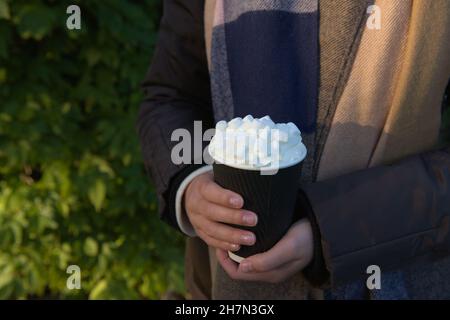 Heiße Getränke zum Mitnehmen für unterwegs in einem Einweg-Becher aus schwarzem und weißem Papier, der recyclingfähig ist. Grün, grün und im Freien Hintergrund spiegelt die Umwelt Stockfoto