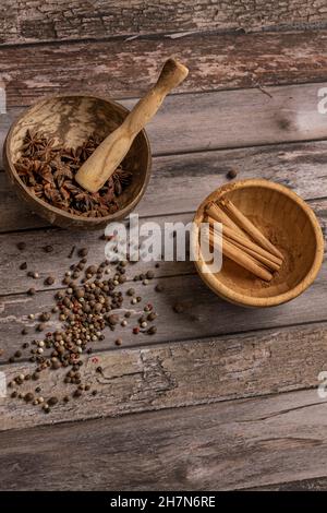 Schüsseln mit Sternanise und Zimt auf altem Plankentisch mit Wacholdersamen und Pfeffer Stockfoto