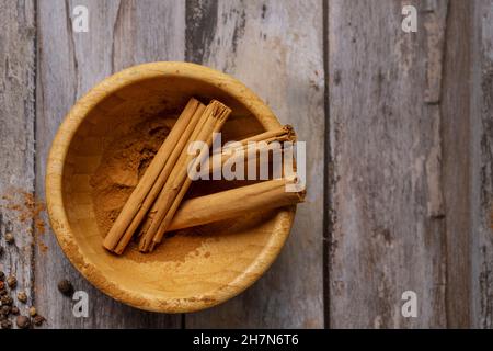 Bambus-Holzschale mit Zimtstangen und gemahlenem Zimt auf einem Vintage-Holztisch Stockfoto