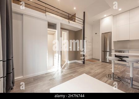 Wohnzimmer in einem Loft mit erhöhtem Schlafzimmer und weißer Küche mit Geräten Stockfoto