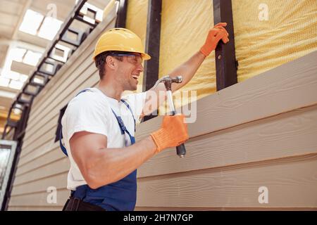Fröhlicher männlicher Baumeister mit Hammer auf der Baustelle Stockfoto