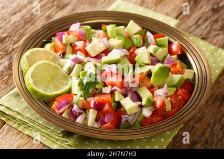 Köstlicher Sommersalat mit Tomaten, Zwiebeln und Avocado in Nahaufnahme auf einem Teller auf dem Tisch. Horizontal Stockfoto