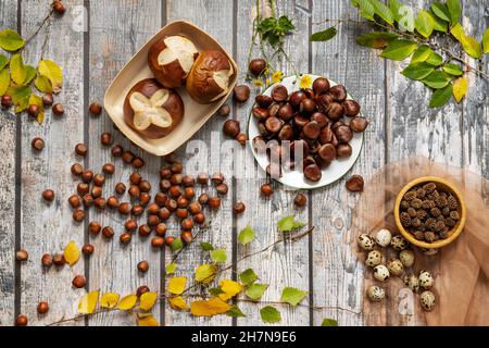 Schönes herbstliches Stillleben mit frisch gebackenen Muffins, rösten Kastanien, Wachteleiern und Haselnüssen mit Laubblättern Stockfoto
