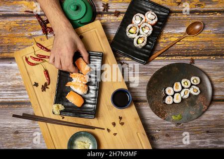 Männerhand hält ein Stück norwegisches Lachs-Nigiri-Sushi aus einer Reihe japanischer Gerichte mit Essstäbchen und Sojasauce Stockfoto