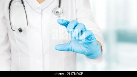 Ärztin, die in medizinischen Handschuhen etwas in ihrer Hand zeigt. Arzt, der Platz für das Produkt oder den Text vorstellt und zeigt. Stockfoto