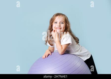 Blauäugiges lockiges Luder mit Grübchen auf ihren Wangen lacht auf dem fliedernen Fitnessball Stockfoto