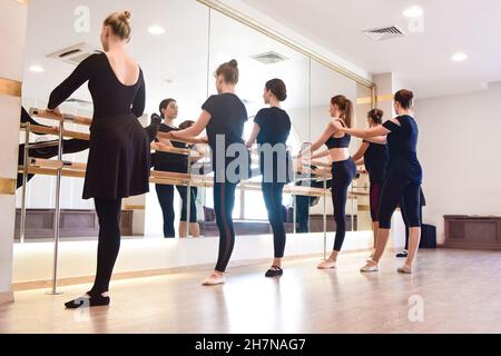 Seitenansicht Gruppen von Mädchen, die in einem Gesundheits- und Fitnesskonzept an der Bar im Fitnessstudio Übungen mit Schwerpunkt auf Sportlichkeit durchführen. Stockfoto