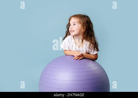 Blauäugiges lockiges Luder mit Grübchen auf ihren Wangen lacht auf dem fliedernen Fitnessball Stockfoto