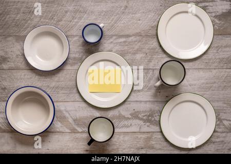 Set aus weiß emaillierten Metallplatten und Tassen mit blauen Kanten auf grauem Holztisch Stockfoto