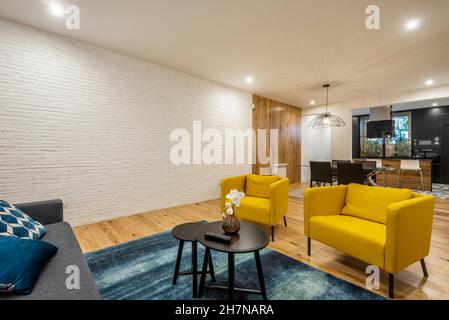 Wohnzimmer mit freiliegenden weißen Backsteinwänden und moderner Einrichtung mit gelben Sesseln und schwarzem Couchtisch Stockfoto