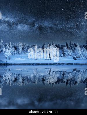 Feenwinternacht. Landschaft mit der Milchstraße und verschneiten Bäumen, die sich im Winter in einem See oder einer Nacht spiegeln. Stockfoto