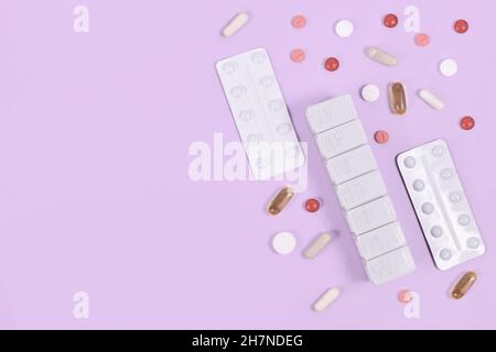 Pillen, Kapseln und Pillenbox auf der Seite mit violettem Hintergrund mit Kopierraum Stockfoto