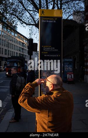 Von hinten betrachtet, überprüft ein Besucher der Hauptstadt am 23rd. November 2021 in London, England, seinen Aufenthaltsort von einem der vielen Kartenposten in der Umgebung Londons, an der Ecke Liverpool Street und Old Broad Street in der City of London, dem Finanzviertel der Hauptstadt. Stockfoto