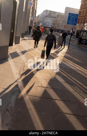 Fußgänger gehen am 23rd. November 2021 in London, England, durch das reflektierte Herbstlicht auf Moorgate in der City of London, dem Finanzviertel der Hauptstadt. Stockfoto