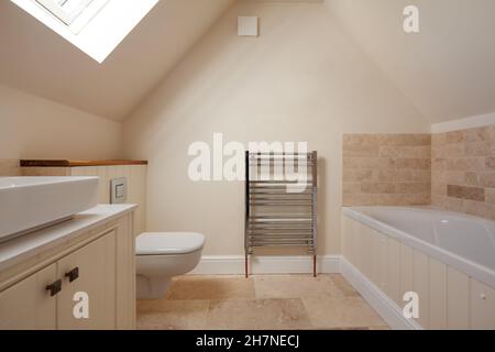 Generische moderne Badezimmer-Suite im traditionellen Stil in leerstehenden neuen Zuhause mit getäfelter Badewanne, Waschbecken, Toilette und teilweise gefliesten Wänden. Stockfoto