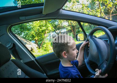 Der vier Jahre alte Junge sitzt hinter dem Steuer und gibt vor, Auto zu fahren Stockfoto