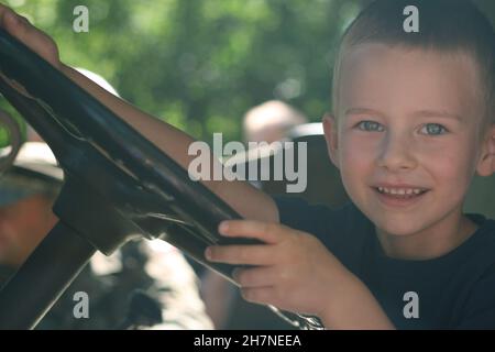 Der vier Jahre alte Junge sitzt hinter dem Steuer und gibt vor, Auto zu fahren Stockfoto