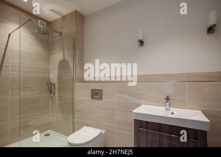 Generisches Duschbad in häuslicher Wohnhausumgebung mit teilweise gefliesten Wänden, Toilette, verglaster Duschkabine und Waschbecken Stockfoto