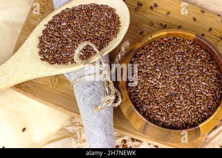 Rohe, trockene Leinsamen in einem Holzlöffel und einer Schüssel auf hellem Hintergrund anbraten. Stockfoto