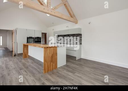 Lolworth, Cambridgeshire - Juli 30 2019: Brandneue, unbesetzte Wohnküche mit gewölbter Decke, Insel-Halbinsel-Einheit und eingebauten Öfen Stockfoto