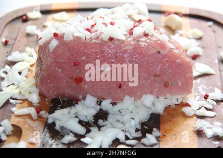 Nahaufnahme des Schweinfilets Mignon, gewürzt mit Gewürzen und Zwiebeln auf einem Holzbrett. Stockfoto