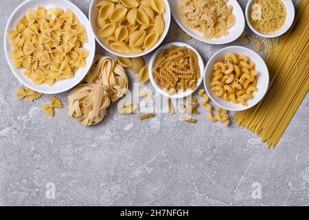 Draufsicht auf verschiedene italienische rohe Pasta in weißer Schale auf grauem Betongrund Stockfoto