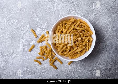 Draufsicht auf italienische rohe Rotini-Pasta in weißer Schale auf grauem Betonhintergrund Stockfoto