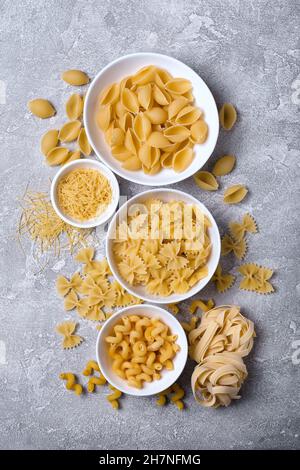 Draufsicht auf verschiedene italienische rohe Pasta in weißer Schale auf grauem Betongrund Stockfoto