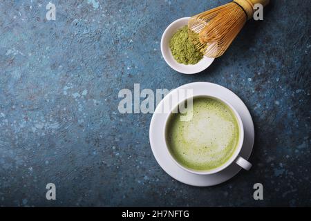 Draufsicht auf grünen Bio-Matcha-Tee oder Latte mit Bambusbesen auf blauem Beton-Hintergrund mit Kopierfläche Stockfoto