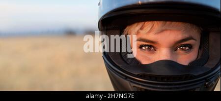 Porträt einer ziemlich blonden Frau Biker Blick auf die Kamera mit ihrem Schutzhelm, um ein Motorrad zu fahren. Hübsche Augen gemacht Stockfoto