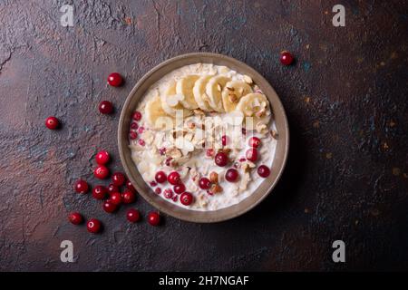 Draufsicht auf Haferflocken mit frischen Preiselbeeren, Haselnüssen, Mandeln und Bananenscheiben für ein gesundes Frühstück auf dunklem Beton Stockfoto