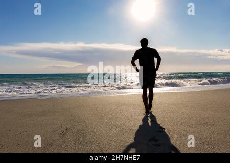 Silhouette eines Mannes, der am Strand gegen das Meer läuft Stockfoto