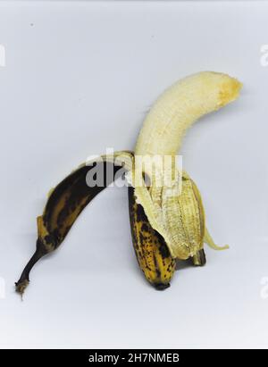 Schneiden Sie das Bild einer überreifen Banane aus, die halb geschält und vor einem weißen Hintergrund steht Stockfoto