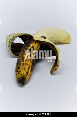 Schneiden Sie das Bild einer überreifen Banane aus, die halb geschält und vor einem weißen Hintergrund steht Stockfoto