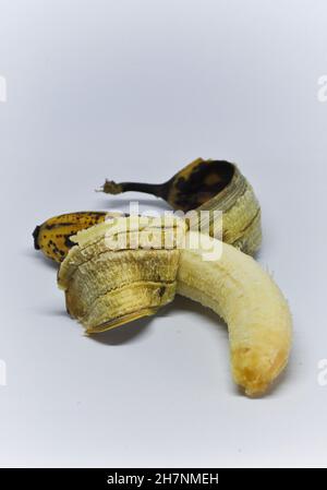 Schneiden Sie das Bild einer überreifen Banane aus, die halb geschält und vor einem weißen Hintergrund steht Stockfoto