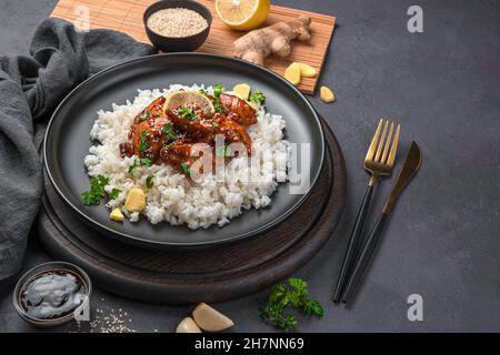 Teriyaki-Huhn mit Reis und Sesam auf einem schwarzen Teller. Stockfoto